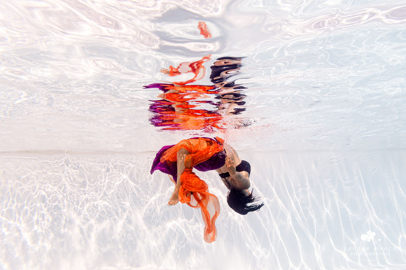 Femme enceinte sous la surface de l'eau, jouant avec le reflet et les voiles colorés orange et violet.