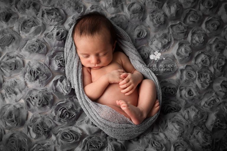 photo de bébé emmailloté dans un tissu douillet et qui dort paisiblement