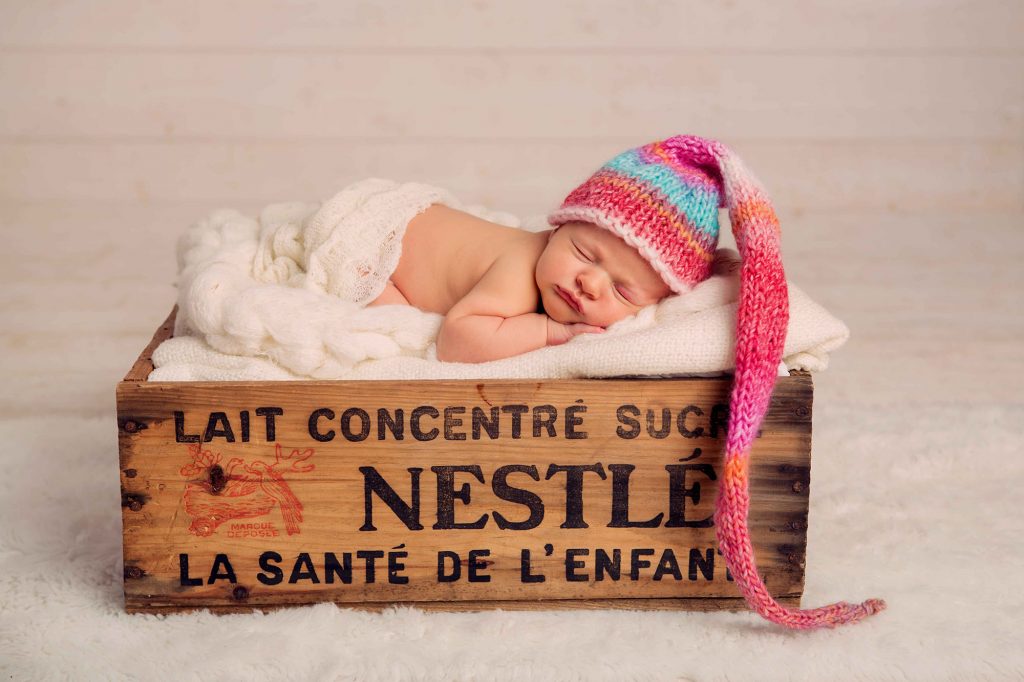 photo newborn d'un bébé endormi dans une caisse nestlé vintage avec un bonnet de lutin rose