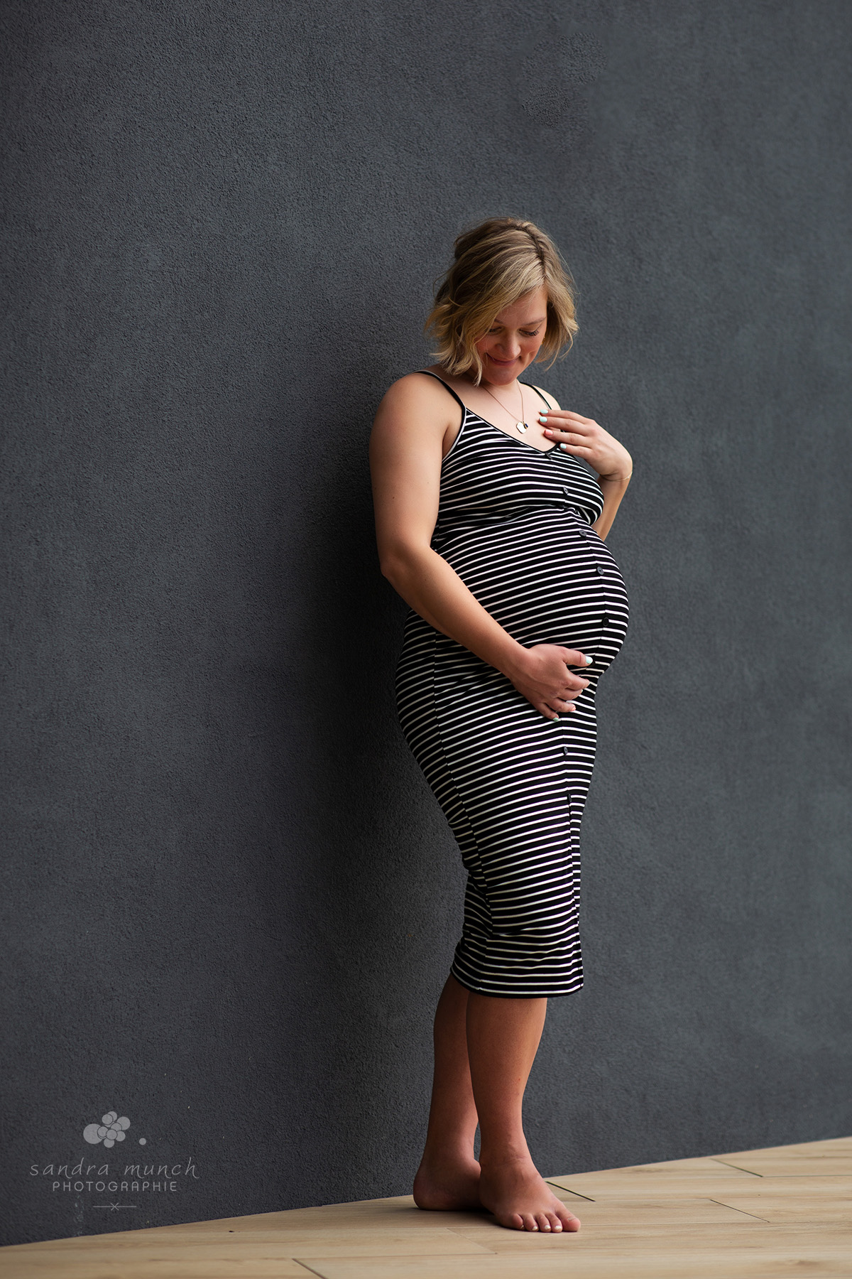 portrait de femme enceinte en robe rayée devant mur gris foncé
