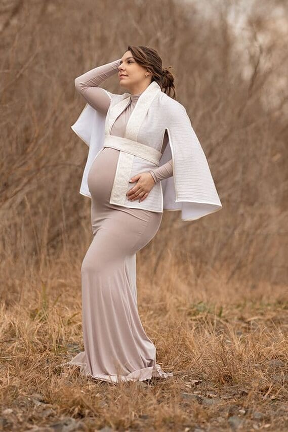 Future maman en robe beige et cape dans un champ en Alsace pour séance photo grossesse