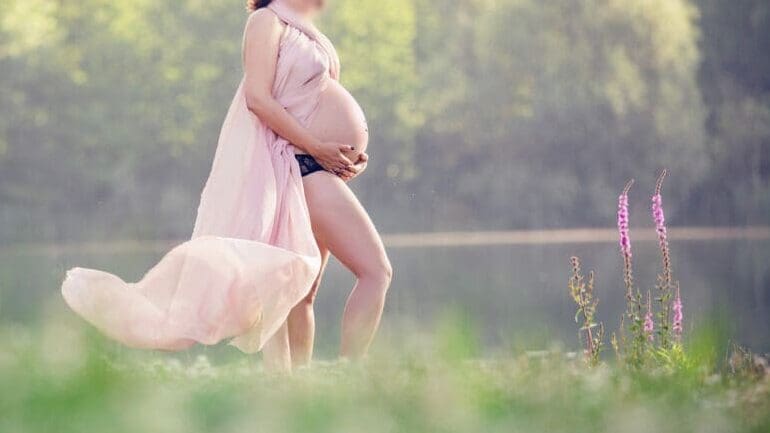 Future maman habillée d'un voile fluide en séance grossesse au lac à strasbourg